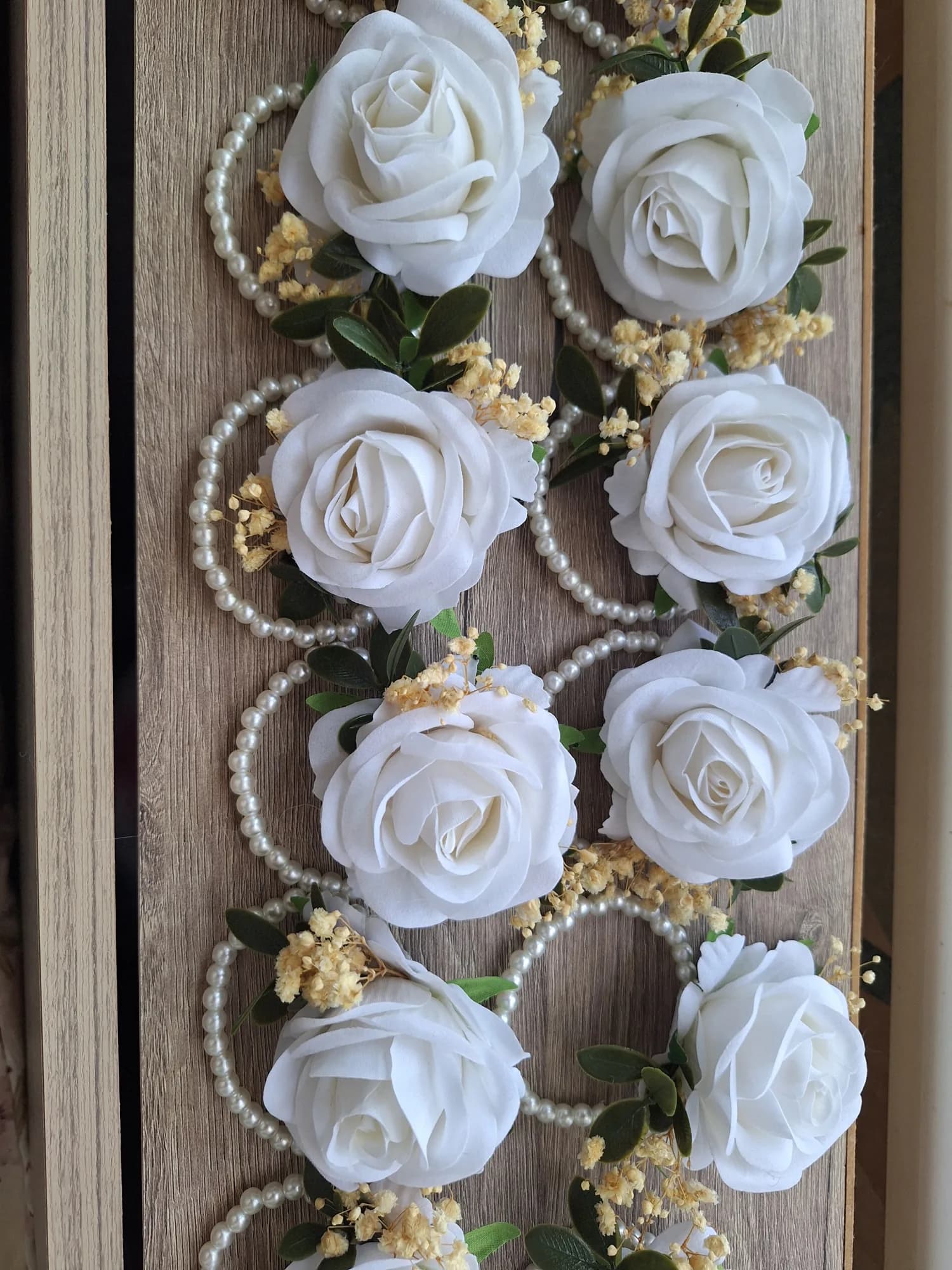 Wrist corsages with white rose, dried gypsophila and green leaves mounted on a pearl-bead bracelet.